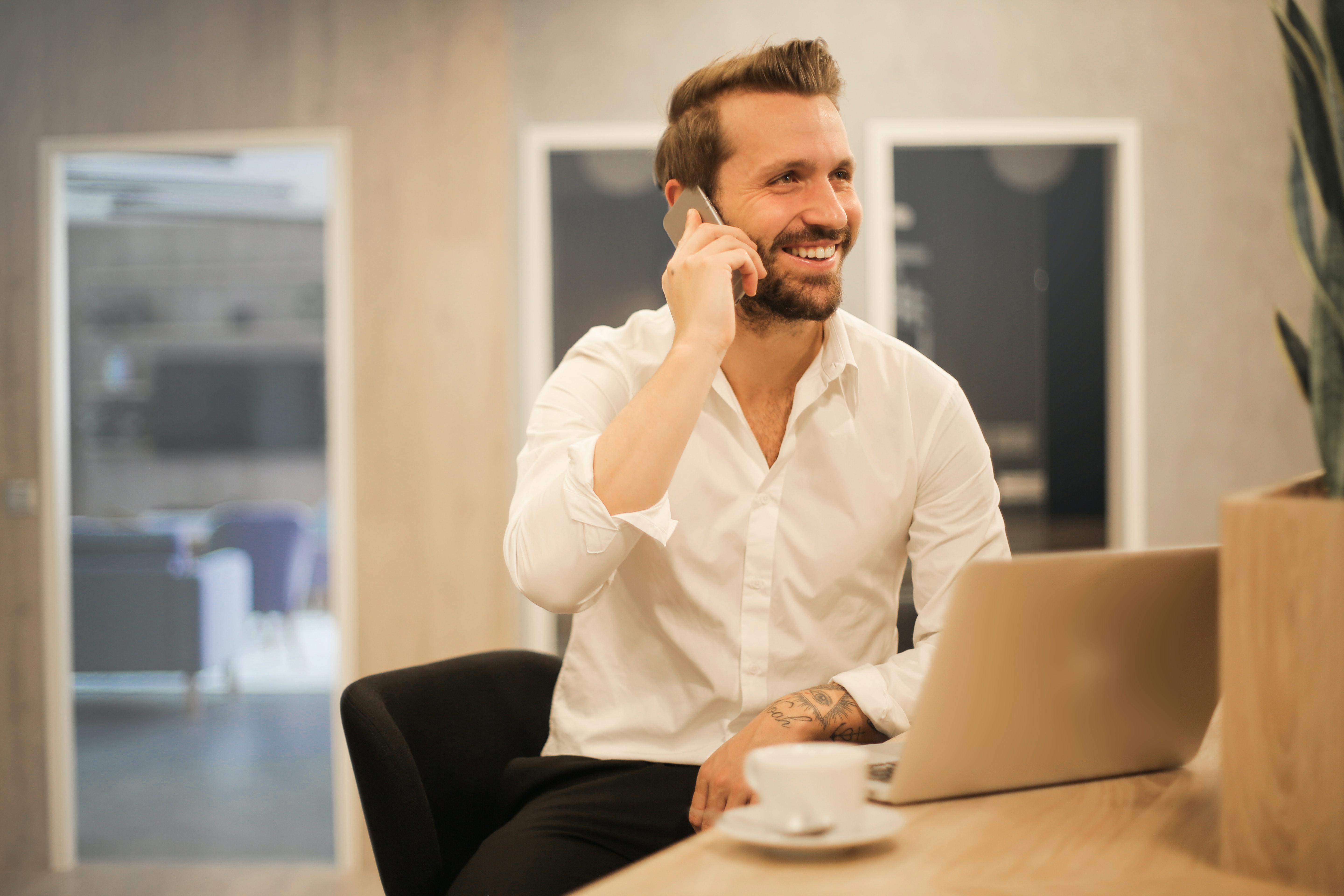 man on mobile phone while working on laptop