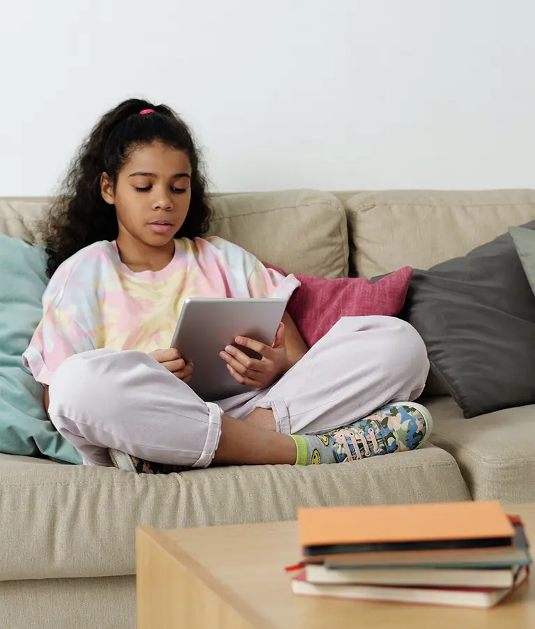 Young girl seated on sofa reading story on tablet device